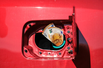 Close up of two fifty euro notes in an open fuel tank on a red car. Raising transportation costs.