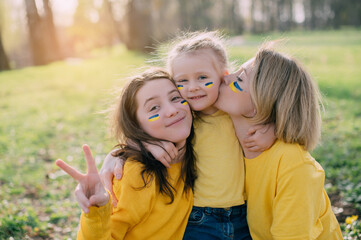 Portrait of Ukrainian family. Mom with two little daughters hugging and smiling in nature on sunny day.