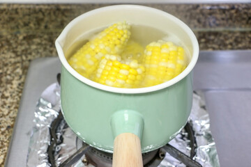 Healthy corn on the cob (sweet corn) stewing and boiling in hot water in a green pot in the kitchen