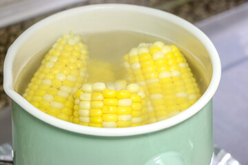 Corn on the cob (sweet corn) boiling in hot water in a green pot