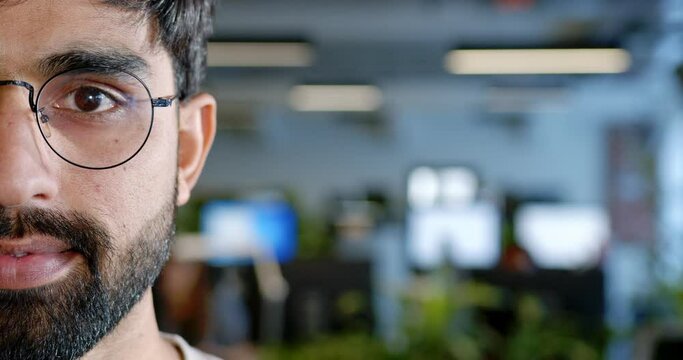 Close up of half of handsome Arabian male face in coworking space. Attractive young man with beard in office interior. Portrait shot. White-collar worker employee in glasses. IT startupper.