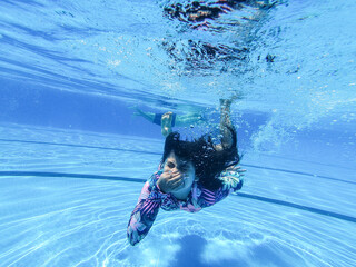little girl creates bubbles under water in the pool.