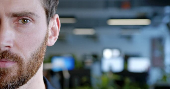 Close up of half of handsome Caucasian male face in coworking space. Attractive young man with beard in office interior. Portrait shot of boss. White-collar worker employee. IT startupper.