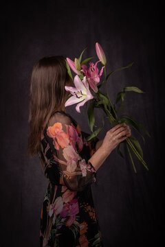 dark classic studio portrait of a woman in floral dress with a bouquet of lily flowers