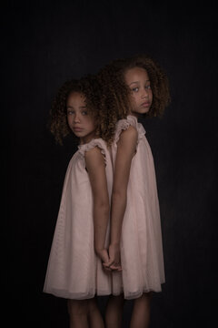 studio portrait of two mixed race girls in white dress in painterly dark style