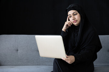 muslim woman using laptop computer and thinking a new idea on sofa and black background