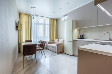 Modern beige and gray stylish kitchen with a table, soft chairs, a sofa and a beige refrigerator. Floor tiles and laminate. Built in household appliance