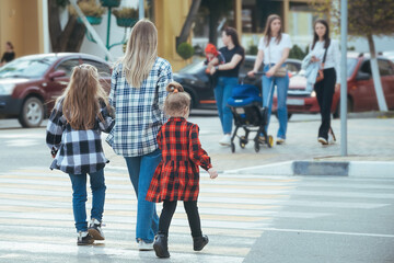 young woman takes two girls across the road in the city. Mom holds her daughters hands and teaches them to cross the road safely at a pedestrian crossing