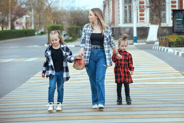 young woman takes two girls across the road in the city. Mom holds her daughters hands and teaches them to cross the road safely at a pedestrian crossing