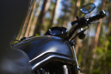 black motorcycle gas tank with protective pipes. out of focus steering wheel, mirror and speedometer against the background of the forest.