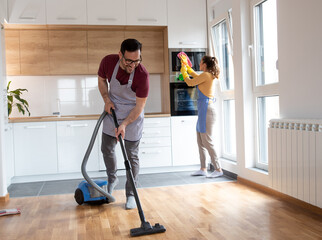 Couple doing chores together vacuuming and cleaning dust in the kitchen.