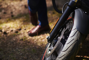 Plakat a perforated motorcycle disc attached to an alloy wheel. Shock absorber with reflector. in the background in defocus are male legs in brown shoes
