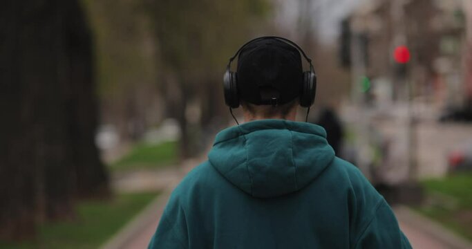 Back view man puts on big headphones walking in the city, slow motion 4k at 120fps