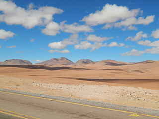  road in the Atacama Desert, with typical yellow colored vegetation, colorful blue sky with clouds . Atacama Desert, Chile, South America