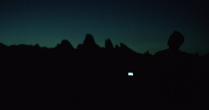 Night sky with moon above mountain silhouettes with man taking photos in Alabama Hills, California