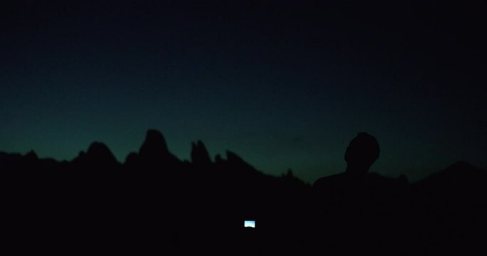 Night sky with moon above mountain silhouettes with man taking photos in Alabama Hills, California