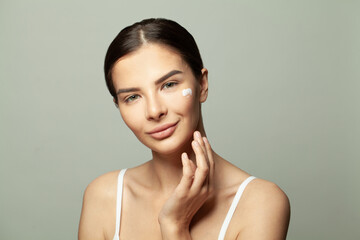 Happy young woman applying moisturizing cream on her face. Photo of pretty spa model with clean...