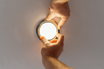 A male electrician changes the light bulbs in the spotlight ceiling lamp