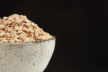 Raw oatmeal grains in a bowl on a black background. Copy space. Shallow depth of field