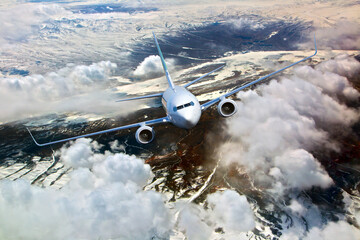 Passenger plane flies above the clouds and mountain landscape. Front view of aircraft.