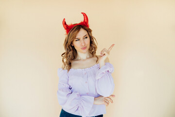 Portrait of a girl with wavy hair, in a devil costume for Halloween near a beige wall.