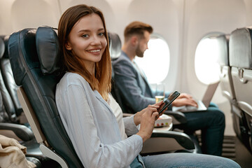 Joyful woman using cellphone in passenger airplane
