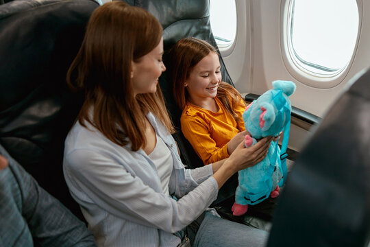 Cheerful mother and daughter playing with toy in airplane