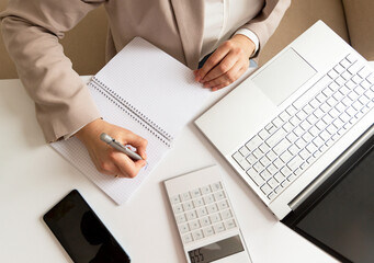 businesswoman counts the budget and makes notes in a notebook on the desktop with a calculator and a laptop.