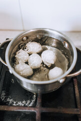Chicken white big eggs are boiled in boiling water in a metal old pan on the stove in the kitchen, top view. Morning breakfast, food photography, concept.