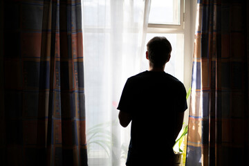 Fototapeta premium back view of man standing in front of the window in the morning at home, silhouette