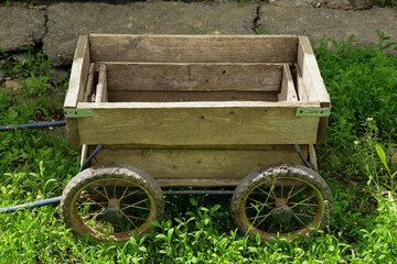 A wooden small empty wagon stands in the green grass