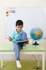 Preschool boy sitting wih book in classroom with globe