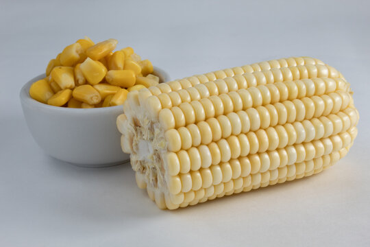 Corn On The Cob Split In Half, Raw And Without Straw, Accompanied By Cooked Corn Kernels, Inside A Ceramic Bowl