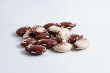 Small portion of raw fava beans in white, brown and red colors scattered on a white background....