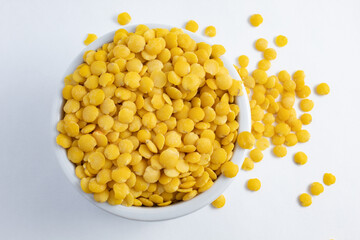 Raw and fresh yellow lentils in ceramic pot viewed from above and with handful scattered on table
