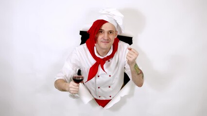 Young handsome man dressed as chef with glass of wine. Male cook dancing with alcoholic beverage and sticking out of hole of white background.