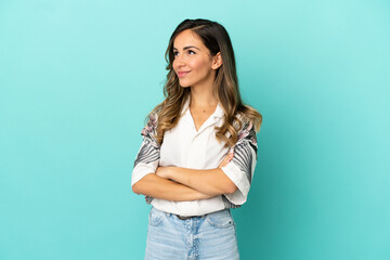 Young woman over isolated blue background looking up while smiling