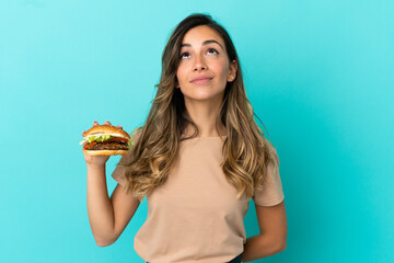 Young woman holding a burger over isolated background and looking up