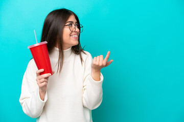 Young caucasian woman drinking soda isolated on blue background intending to realizes the solution while lifting a finger up