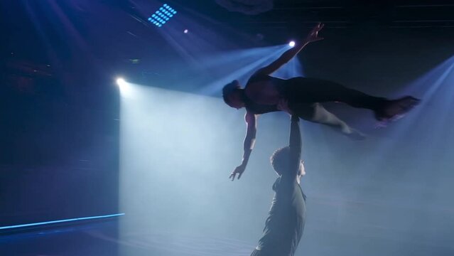 Risky forbidden overhead lift in figure skating, slow motion.Skaters couple make stationary rotational support. Man holds woman parallel to ice on his one straight hand,her legs in split of 45 degree.