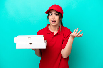 Pizza delivery woman with work uniform picking up pizza boxes isolated on blue background with shocked facial expression