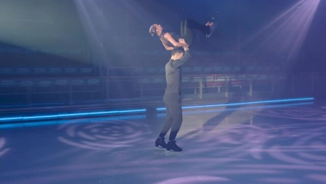 Figure skater moving backwards lifts female partner by waist, makes throw, helping to make back flip from overhead support, woman lands on ice. Complex figures in skating. Very slow motion full HD .