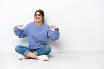 Young caucasian woman sitting on the floor isolated on white background proud and self-satisfied