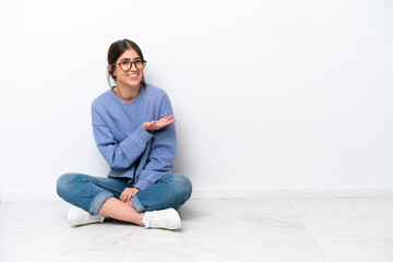 Young caucasian woman sitting on the floor isolated on white background presenting an idea while looking smiling towards