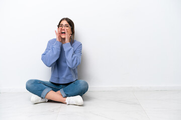 Young caucasian woman sitting on the floor isolated on white background shouting and announcing...