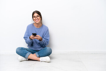 Young caucasian woman sitting on the floor isolated on white background sending a message with the...