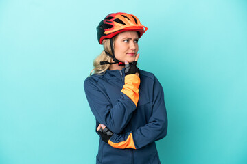 Young cyclist woman isolated on blue background having doubts