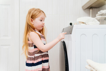 a cute little girl independently turns on the washing machine. 