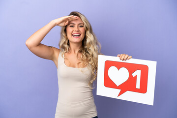 Young Brazilian woman isolated on purple background holding a placard with Like icon with surprised expression