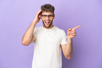 Delivery caucasian man isolated on purple background surprised and pointing finger to the side